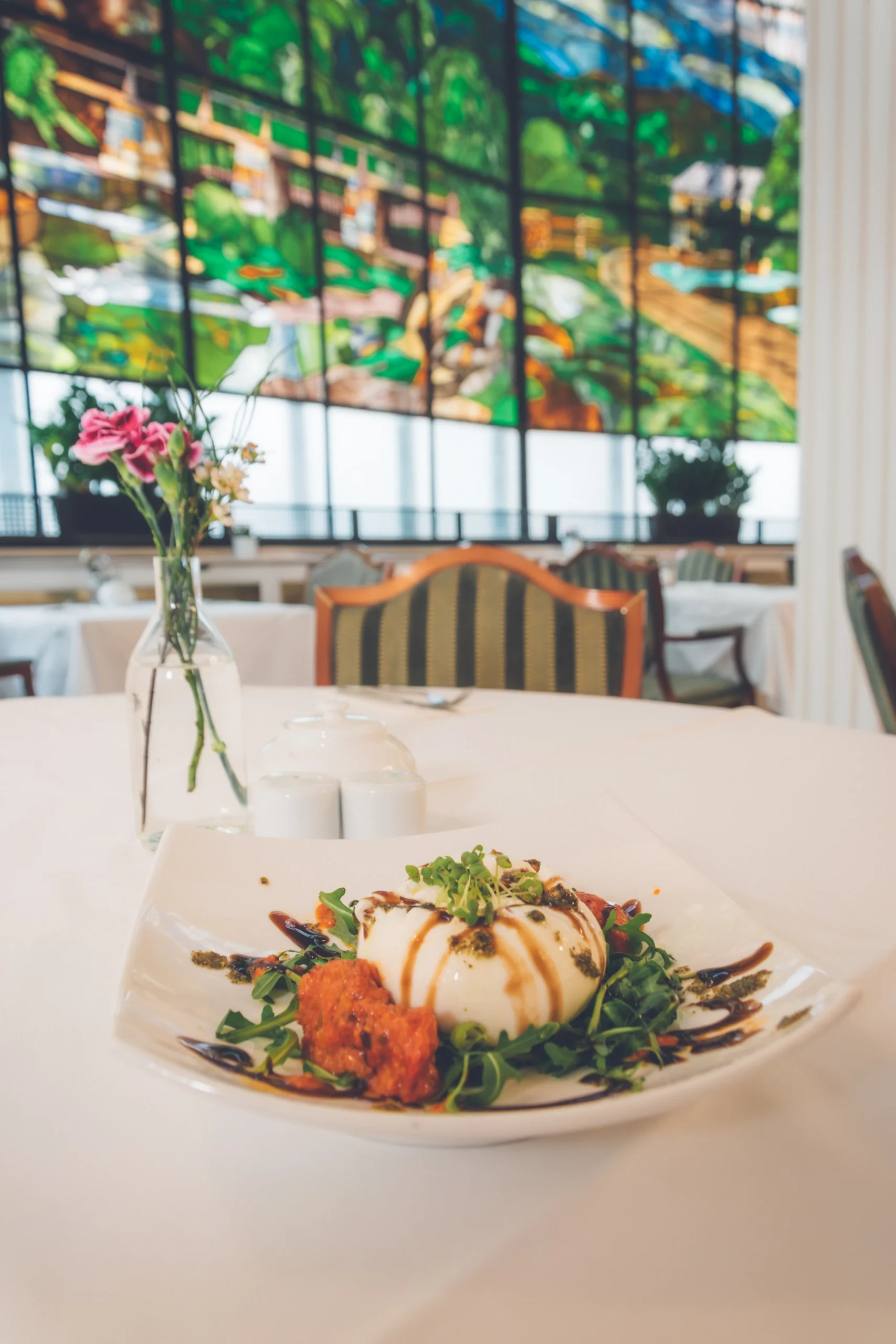 Elegante Burrata-Vorspeise serviert auf frischem Rucola mit Balsamico-Reduktion und Topping im Restaurant derFerdinand in Baden. Kulinarische Gastronomie mit italienischen Einflüssen und stilvoller Präsentation auf weißem Tischtuch.