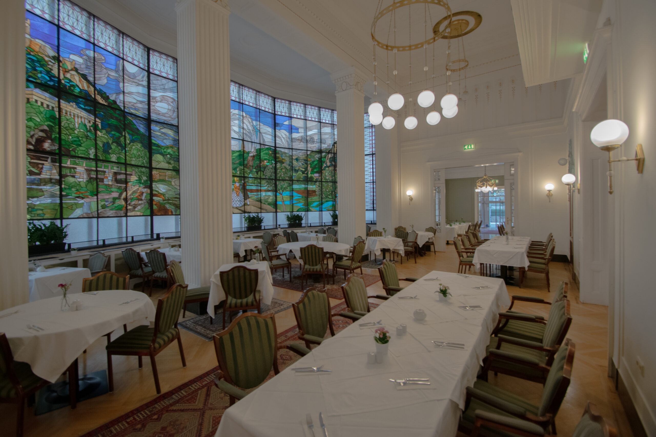 Eleganter Restaurantraum mit hohen Decken, bunten Glasfenstern und festlich gedeckten Tischen im derferdinand Baden
