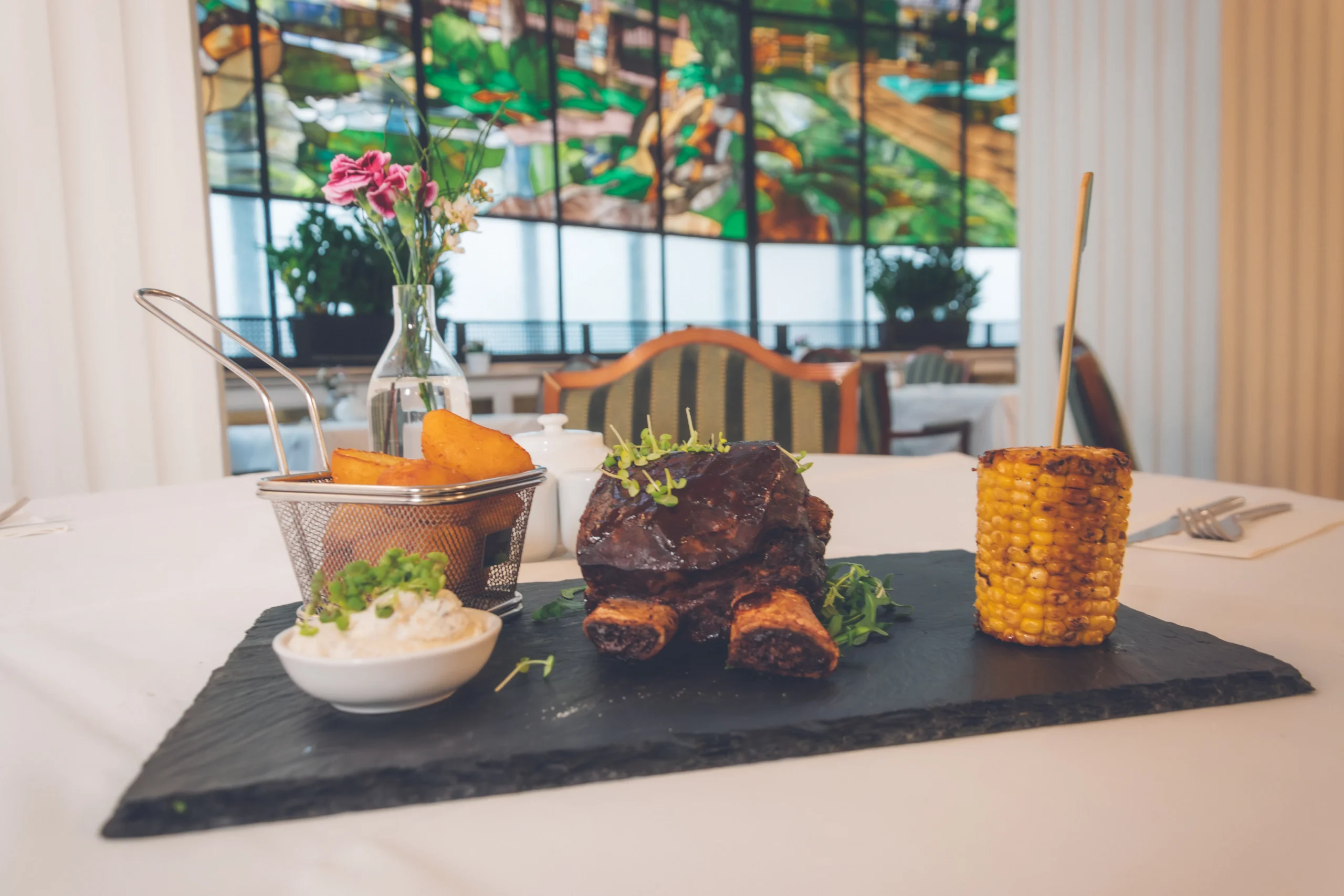 Gegrilltes Fleischgericht mit Maiskolben und Beilagen auf Schieferplatte im Restaurant derFerdinand Baden